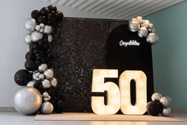 panel de lentejuela negro con números rellenos de luces y globos negros y plateados para decoración cumpleaños 50